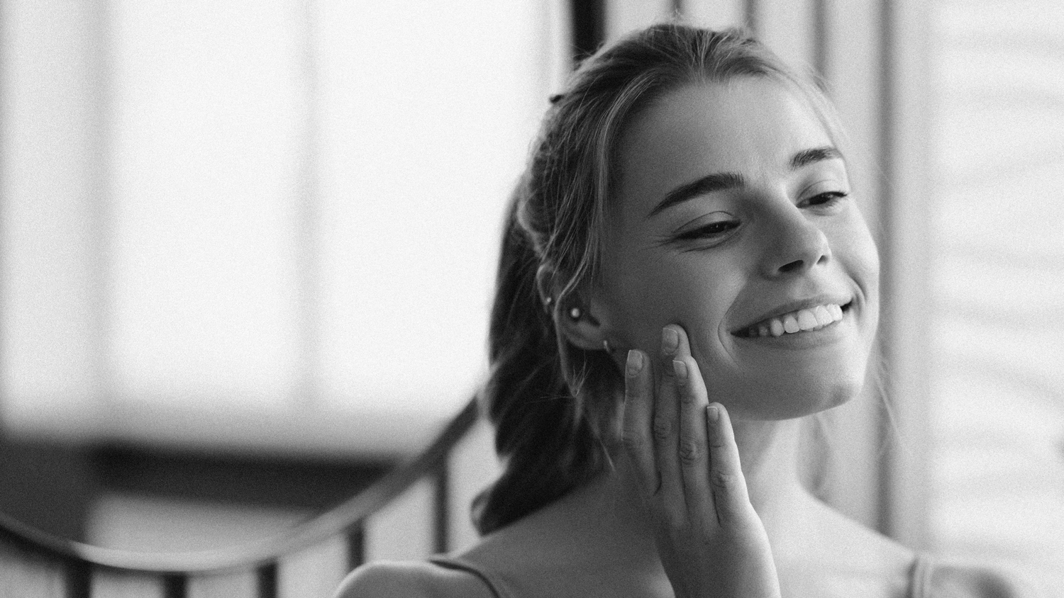 Young women looking in mirror at face with hand on face