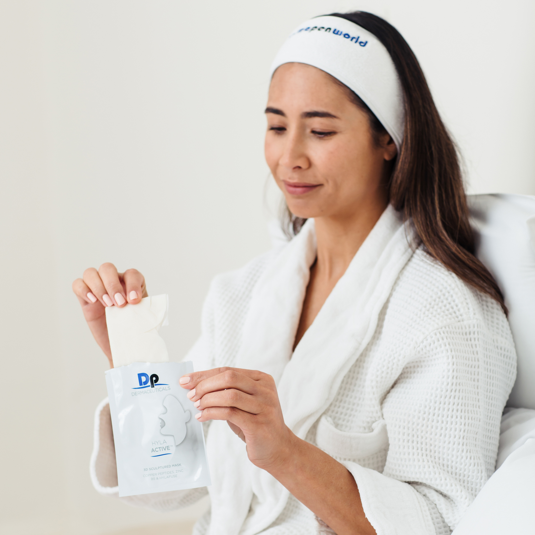 Woman holding Dp Dermaceuticals 3D Sculptured Mask in hand, wearing a white robe and head band