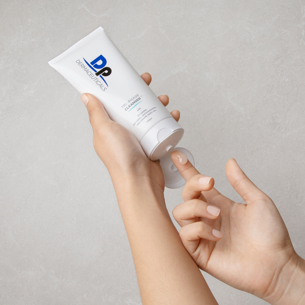 Dp Dermaceuticals Tri-Phase Cleanser being applied to hands in front of a grey background