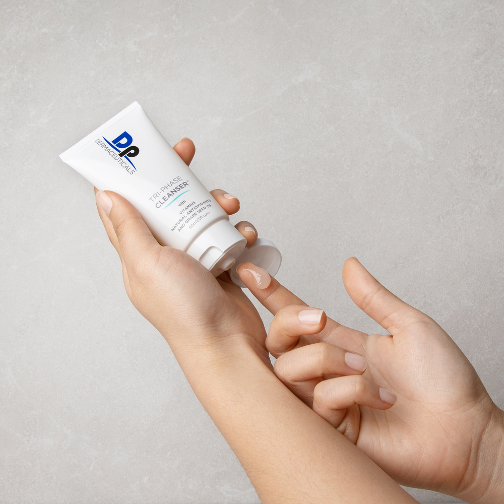 Dp Dermaceuticals Tri-Phase Cleanser in persons hand, squeezing out product
