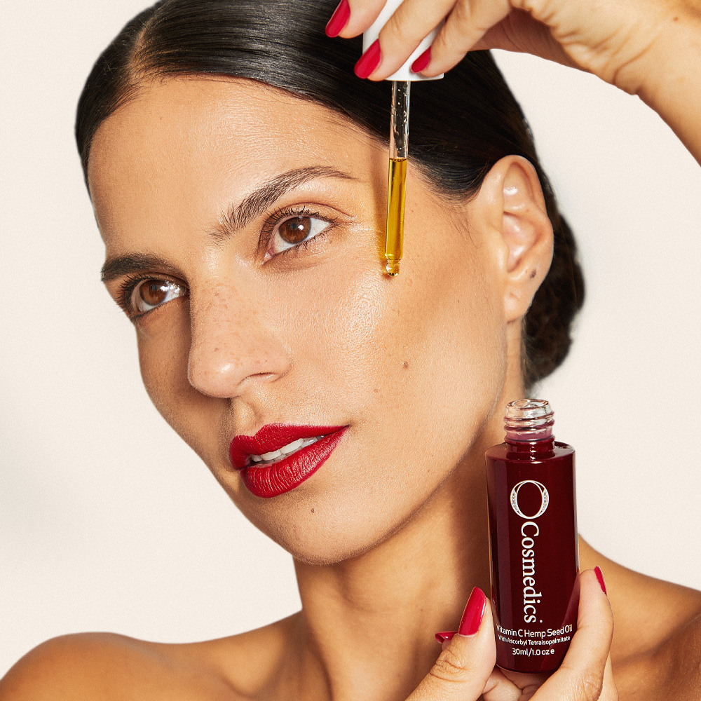 dark haired woman applying o cosmedics vitamin c hemp seed oil to face